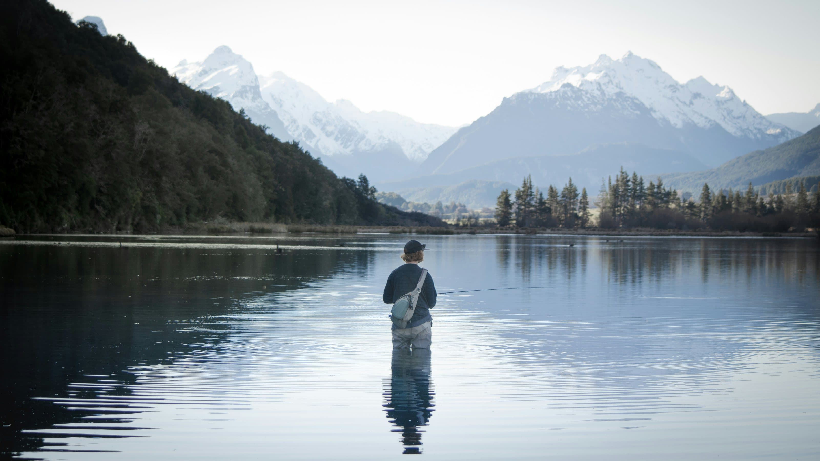 Pescador con mosca lanzando en un lago de montaña al amanecer